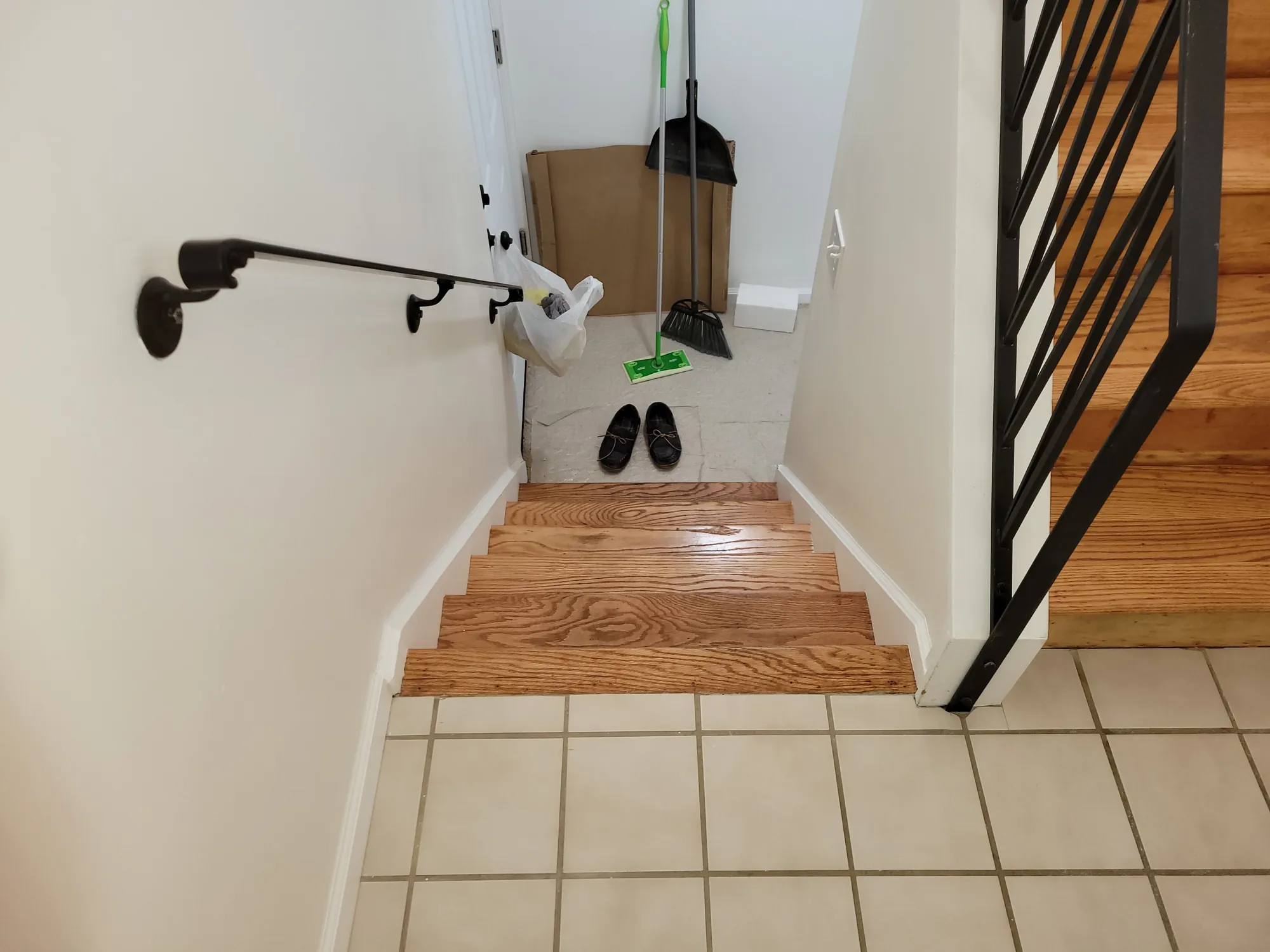Wood stair treads and tile entry beside a black metal railing