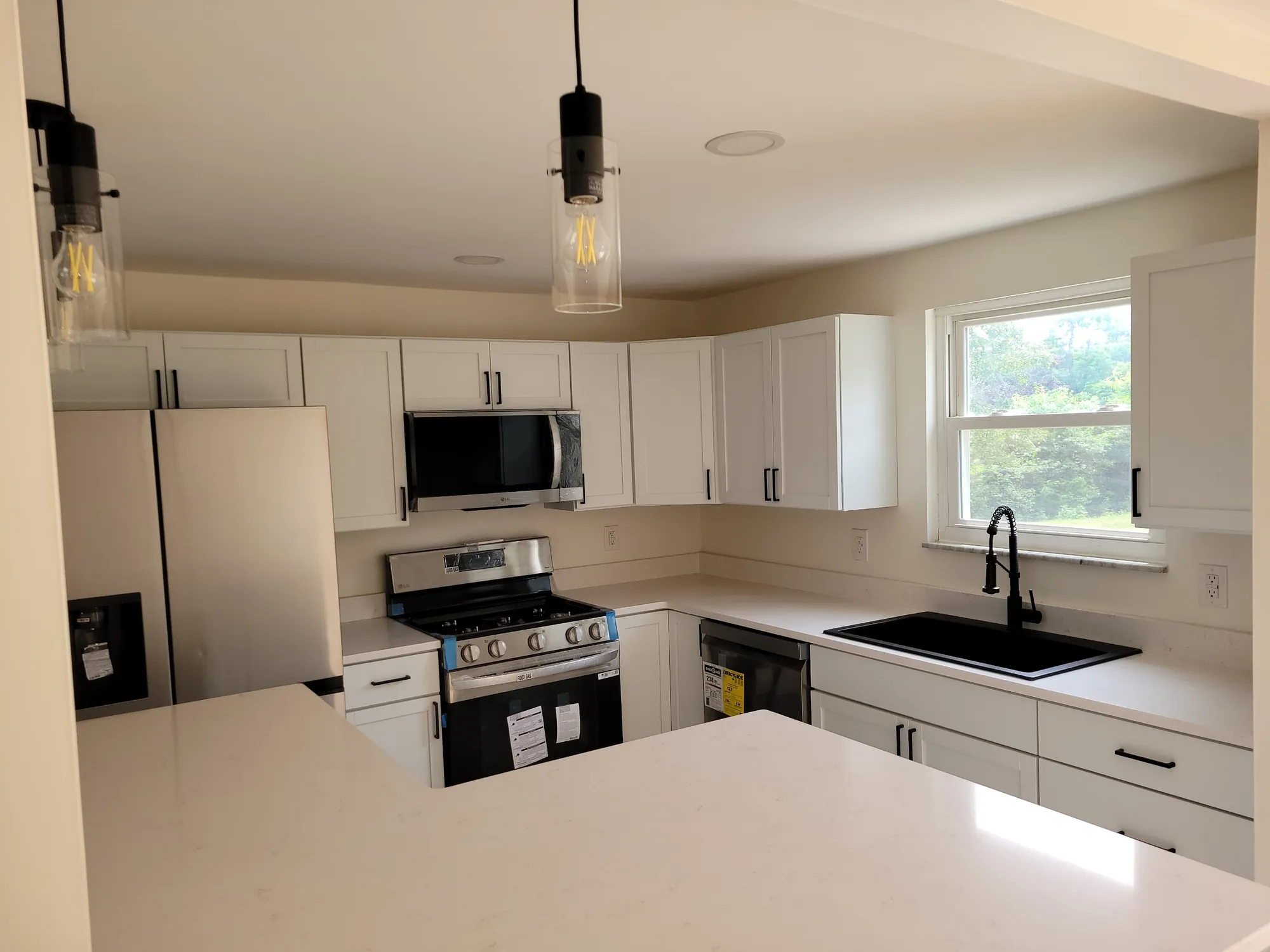 Renovated kitchen with white cabinets, quartz counters and pendant lights
