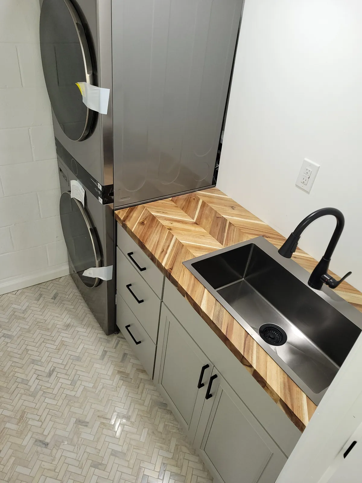 Laundry nook with a butcher block vanity, black sink and herringbone tile floor